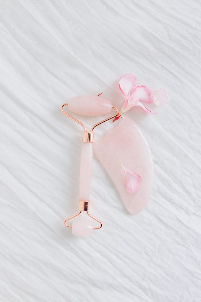 services-02 A rose quartz gua sha and roller set with pink petals, perfect for beauty and skincare routines.